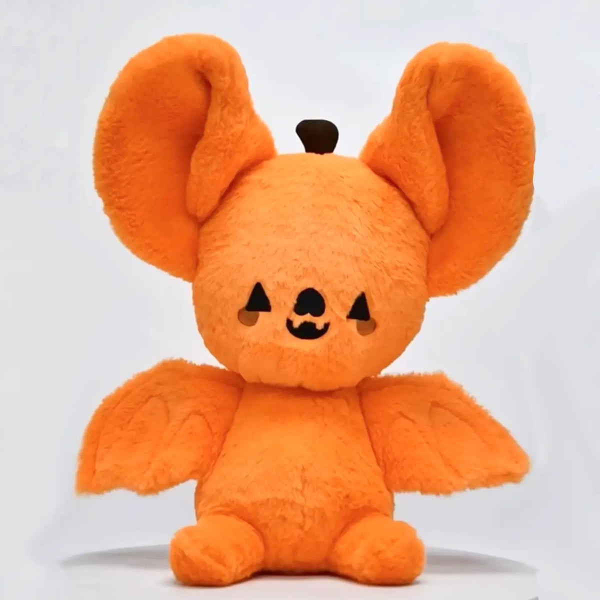 Orange pumpkin bat plushie with oversized ears, spread wings, an embroidered face, and a brown stem on a white background.